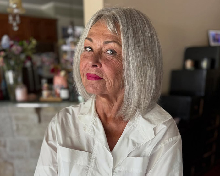 A portrait of a woman with short silver hair wearing bright pink lipstick and a white shirt.