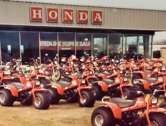 A nostalgic photo of red Honda three-wheel ATVs parked in front of a dealership for 80s kids.