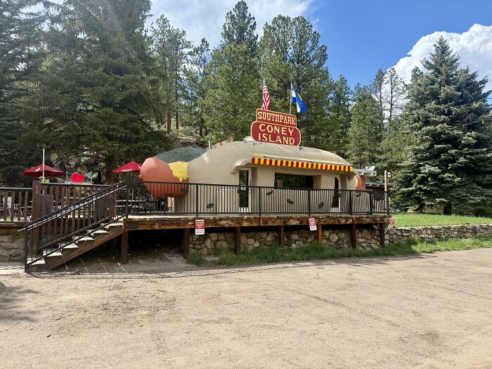 Quirky hot dog shaped building with outdoor seating in wooded area