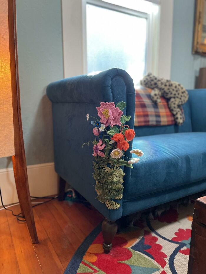 A blue velvet couch decorated with crocheted flowers on the armrest displaying creativity.