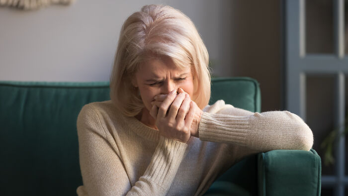 An older woman crying on a green sofa, illustrating the emotional pain of being disowned by family.
