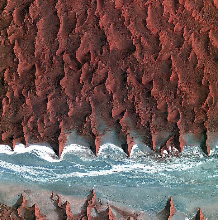 Surreal satellite photos capturing dramatic red sand dunes meeting blue water in a desert landscape.