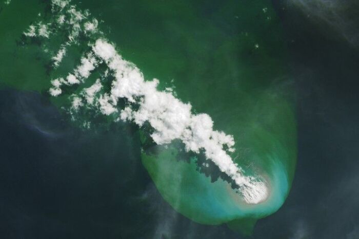 Surreal satellite photos revealing a plume of volcanic steam rising above a vibrant turquoise sea.