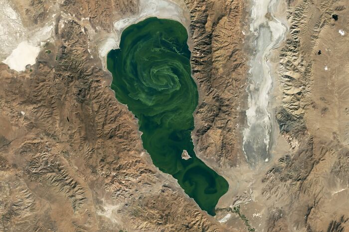 Surreal satellite photo showing a swirling green lake nestled amidst rugged desert mountains.