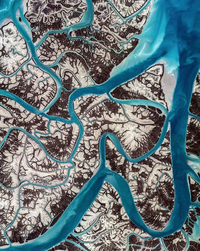 Surreal satellite photo featuring winding turquoise river channels carving through a stark, frosty landscape.