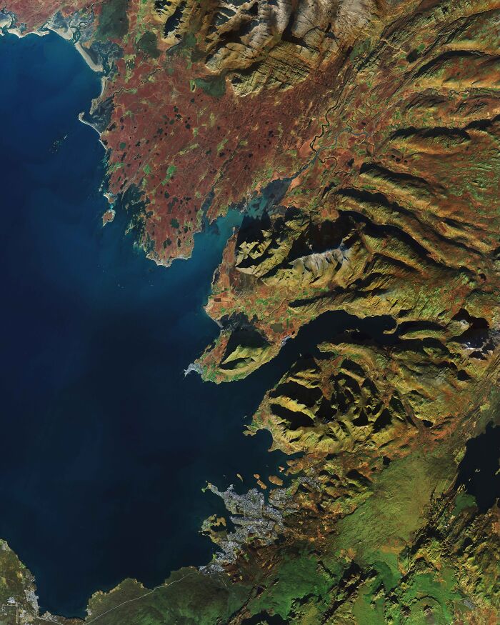 Surreal satellite photo of a dramatic coast line with rugged mountains bordering deep blue ocean waters.