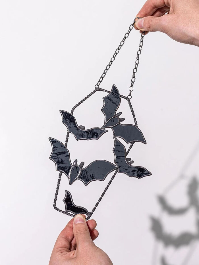 Hand holding a black stained glass bat suncatcher hanging decoration for Halloween.