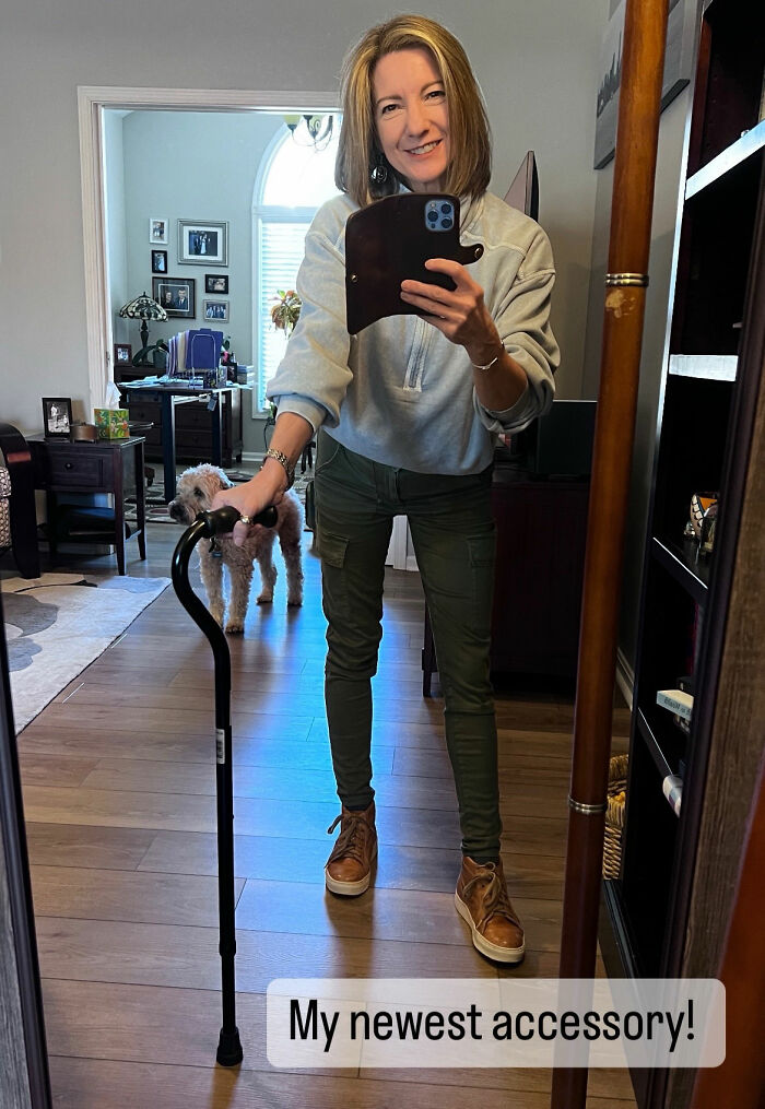 Woman taking a mirror selfie at home while holding a black walking cane as a stylish mobility aid.