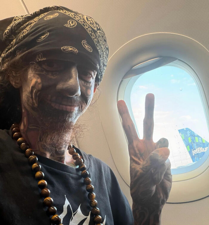 Florida demonologist with extensive face tattoos smiling and making a peace sign on a plane Florida demonologist with extensive face tattoos smiling and making a peace sign on a plane