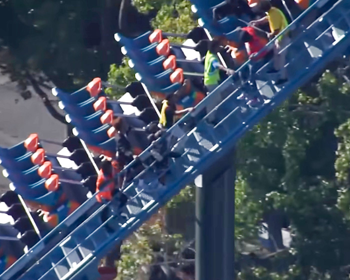 An overhead view of staff assisting passengers on a Six Flags roller coaster train. An overhead view of staff assisting passengers on a Six Flags roller coaster train.