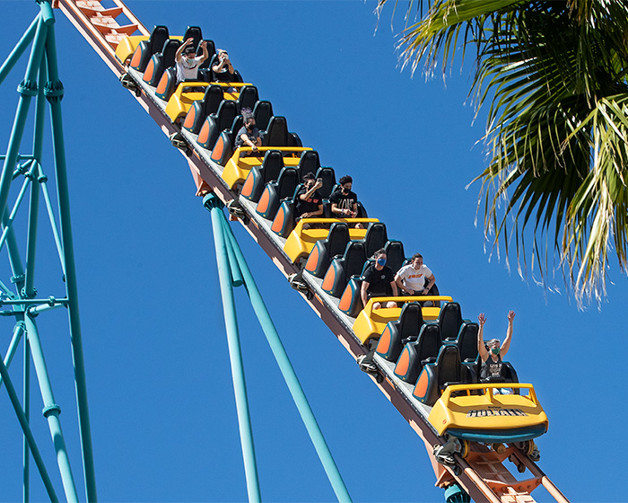 People riding a yellow and teal Six Flags roller coaster climbing a steep track. People riding a yellow and teal Six Flags roller coaster climbing a steep track.