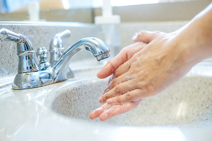 Close-up of hands being washed with soap at a sink, representing hygiene tips for travelers stopped by TSA