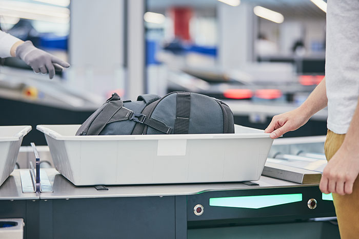 A traveler placing a backpack in a bin at airport security checkpoint
