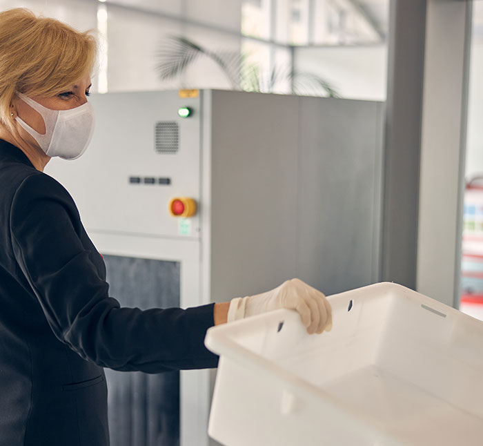 TSA officer wearing a face mask and gloves holding a security bin for travelers