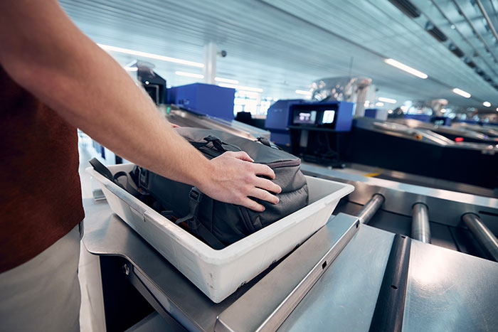 Traveler placing a backpack into a plastic tray on a conveyor belt for TSA screening
