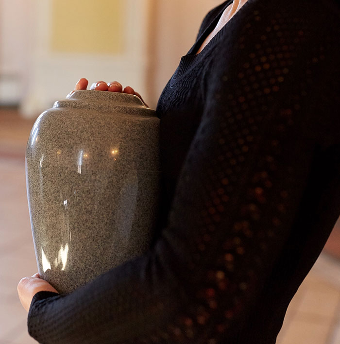 A person in black clothing holds a stone cremation urn, highlighting items carried by travelers stopped by TSA