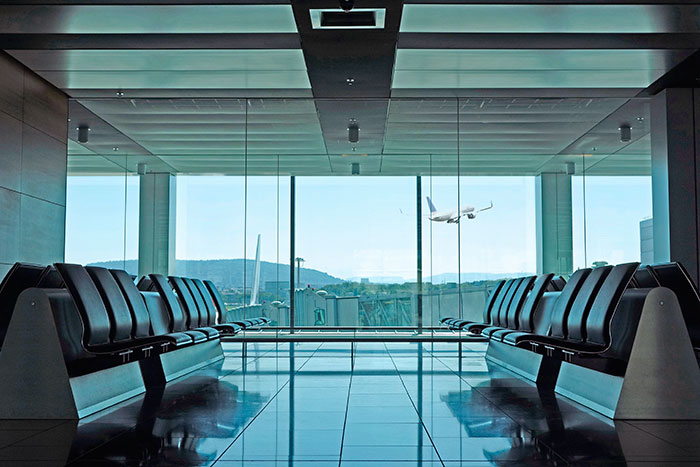 Empty airport terminal seats looking out at an airplane taking off, highlighting travelers stopped by TSA