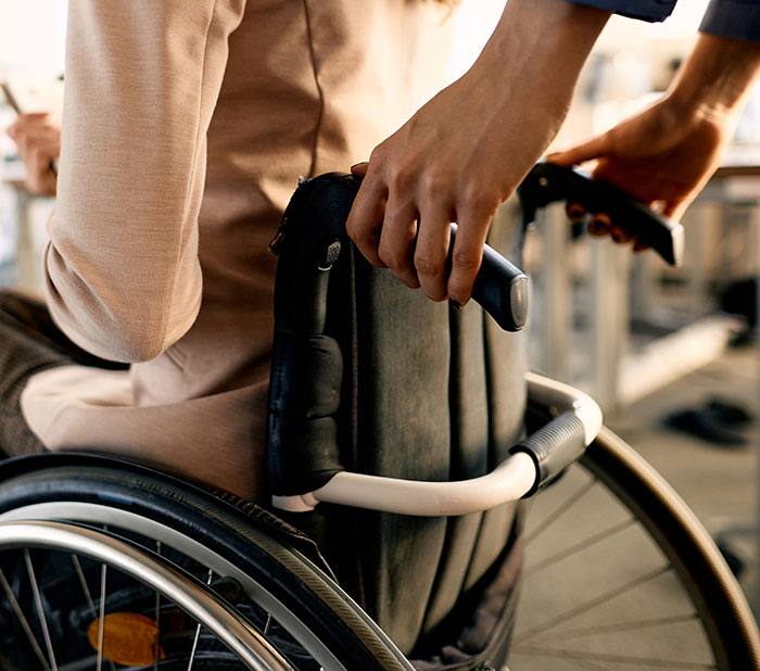 Hands pushing a traveler in a wheelchair, depicting accessibility situations where people are stopped by TSA.