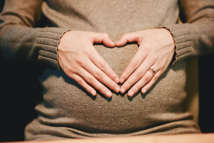 Pregnant woman forming a heart shape with her hands over her belly, reflecting topics on narcissistic parents.