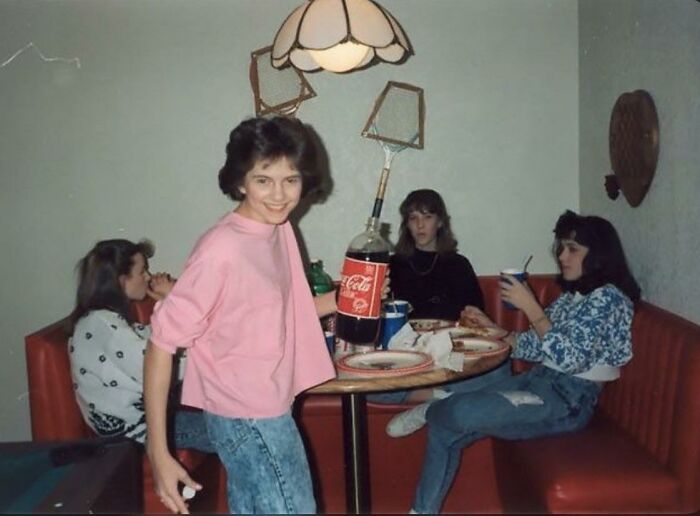 Teenagers hanging out in a booth with a 2-liter Coca-Cola bottle in one of these nostalgic photos of 80s kids.