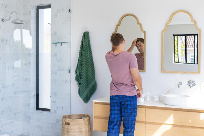 A man fixes his hair in a bathroom mirror, highlighting things about living with guys.