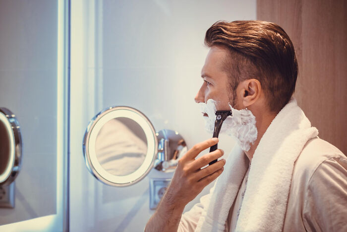 A man shaving his beard in front of a mirror, a daily routine when living with guys