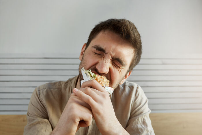 A man eagerly biting into a burger, showcasing living with guys habits