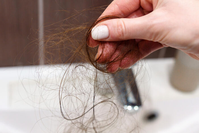 A hand holding a clump of hair over a white sink, symbolizing surprise about living with guys.