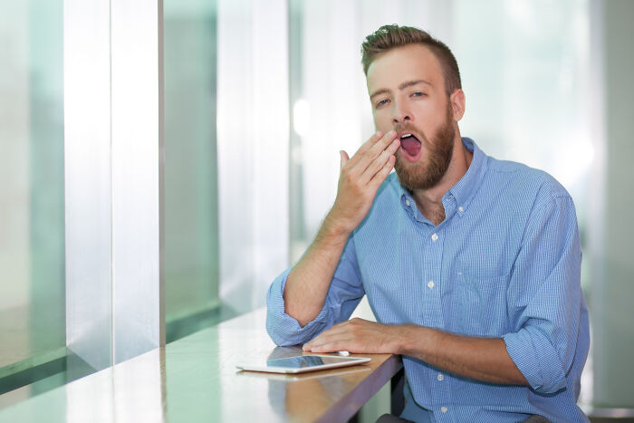 Tired young man yawning at a desk, showing another side of living with guys