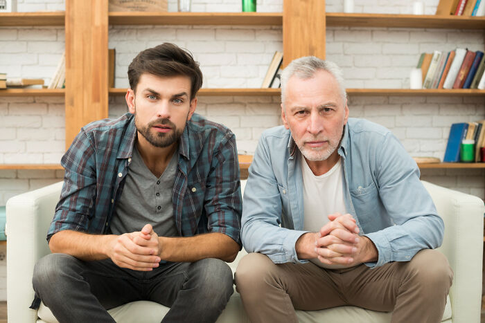 Two serious men sitting on a couch, illustrating different perspectives on living with guys