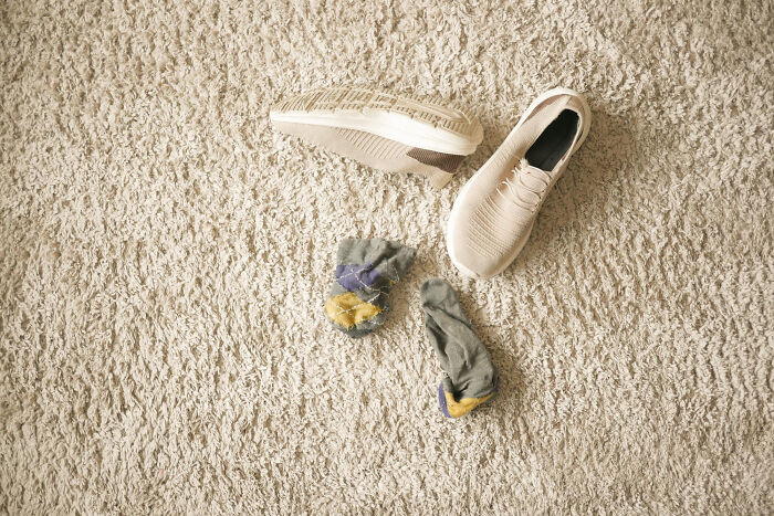 Shoes and worn socks left messy on a carpeted floor, showing a classic habit of living with guys.