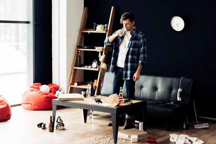 Man drinking water in messy living room, highlighting the reality of living with guys