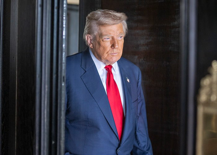 Donald Trump in a blue suit and red tie walking through a doorway near discussion on Susan Dell transformation.
