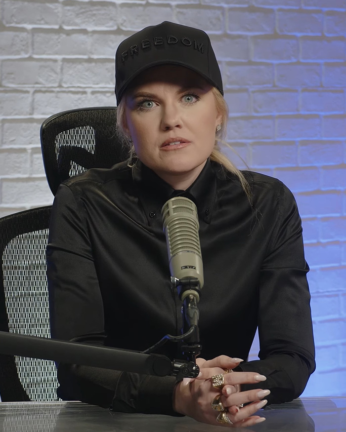 Erika Kirk wearing a black Freedom hat and dark shirt at a podcast microphone.