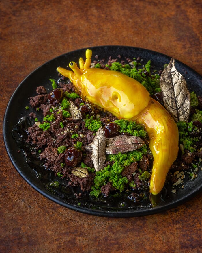 Creative yellow slug dessert served over chocolate crumbs representing creative Halloween foods on a black plate.