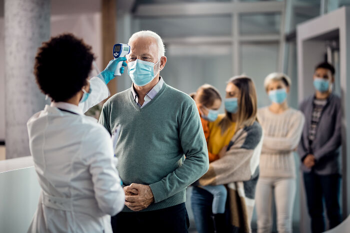 Medical professional checking temperature of elderly man in health threat assessment line