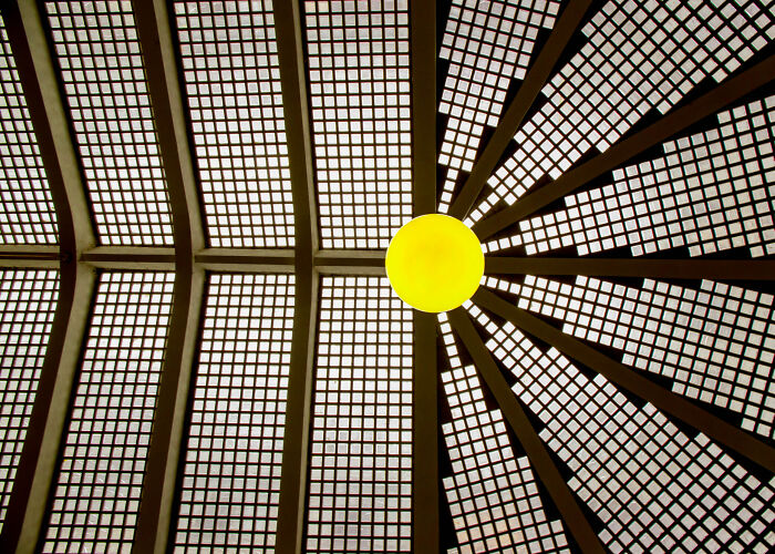 A glowing yellow light under a geometric glass ceiling highlighting the hidden beauty of buildings