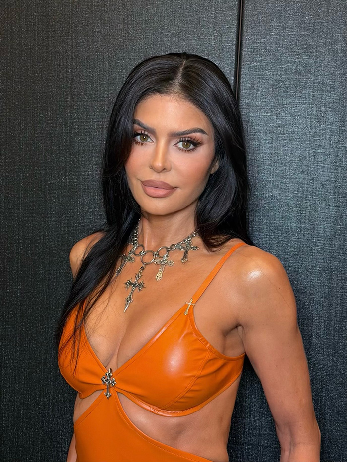 Woman with dark hair in orange crop top and silver cross necklace as celebrity Halloween costume