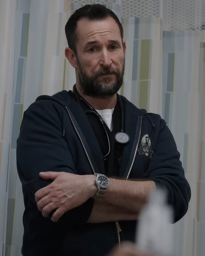 Noah Wyle from The Pitt standing with crossed arms in scrubs and a hoodie Noah Wyle from The Pitt standing with crossed arms in scrubs and a hoodie