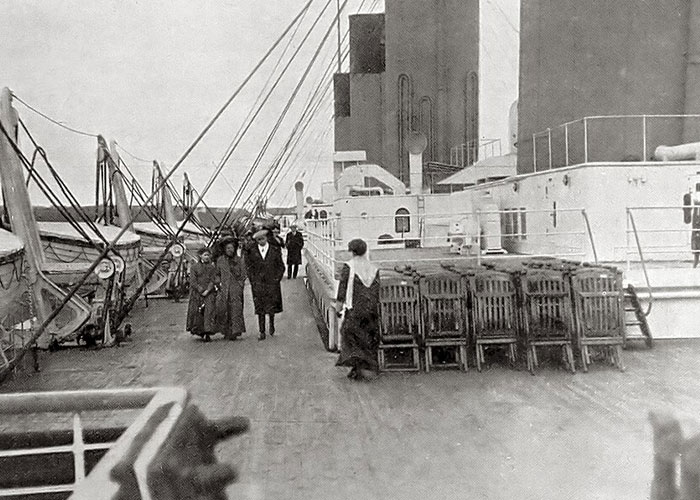 Historical photo of passengers walking along the deck of the Titanic near lifeboats. Historical photo of passengers walking along the deck of the Titanic near lifeboats.