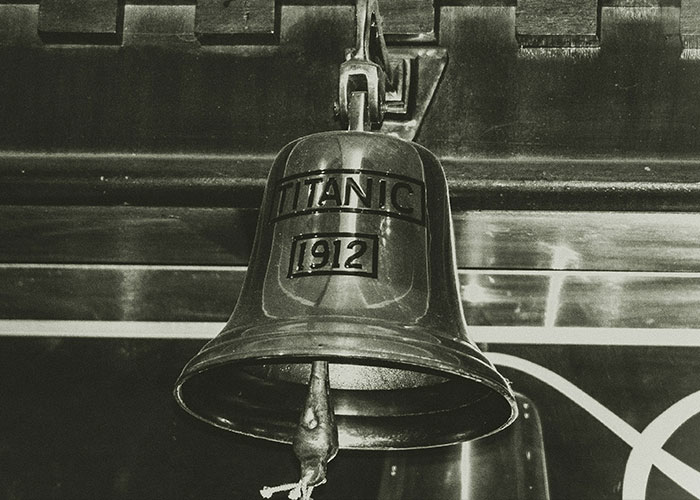 Close-up of a brass ship bell engraved with Titanic 1912 hanging indoors. Close-up of a brass ship bell engraved with Titanic 1912 hanging indoors.