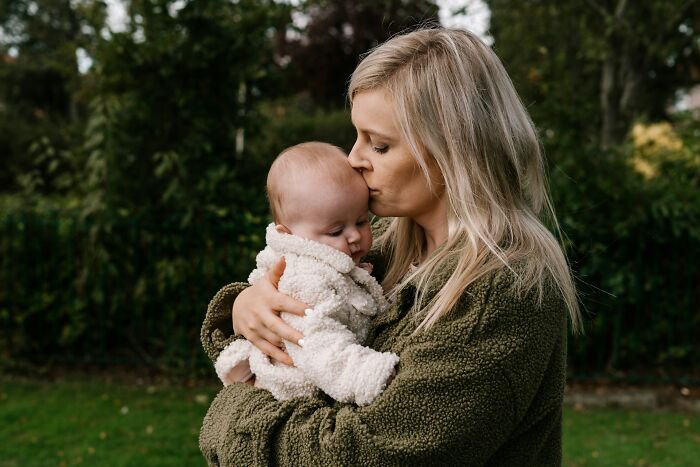 A mother holding and kissing her baby outside, showing family moments that avoid Halloween conflicts.