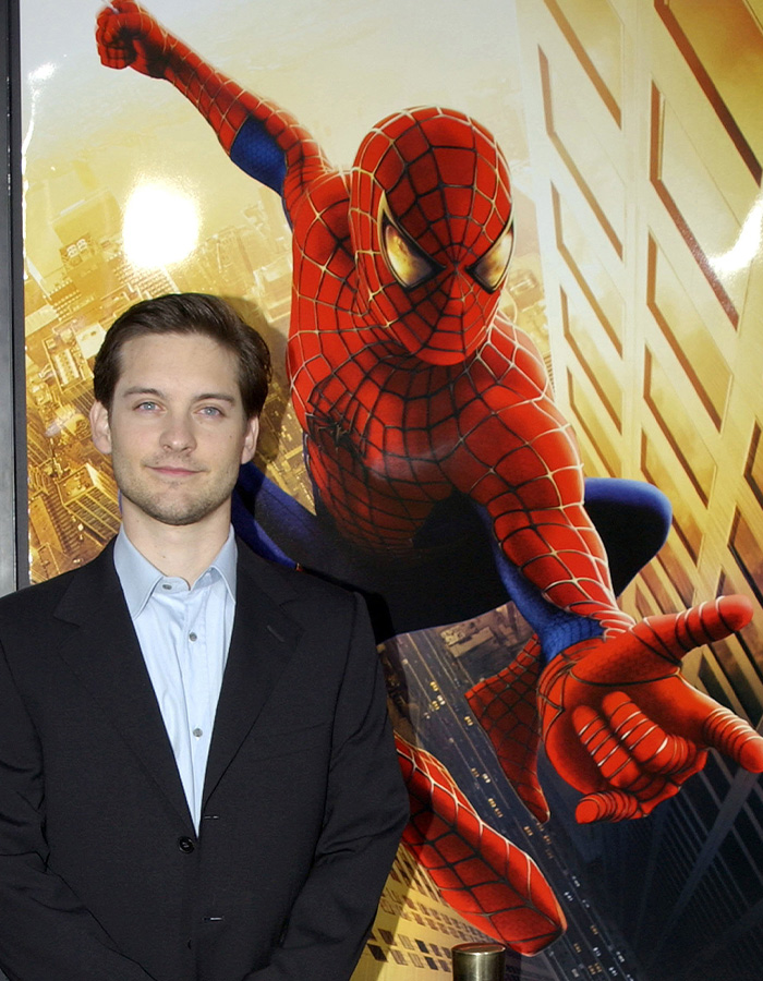 Tobey Maguire standing in front of a movie poster of him as Spider-Man Tobey Maguire standing in front of a movie poster of him as Spider-Man