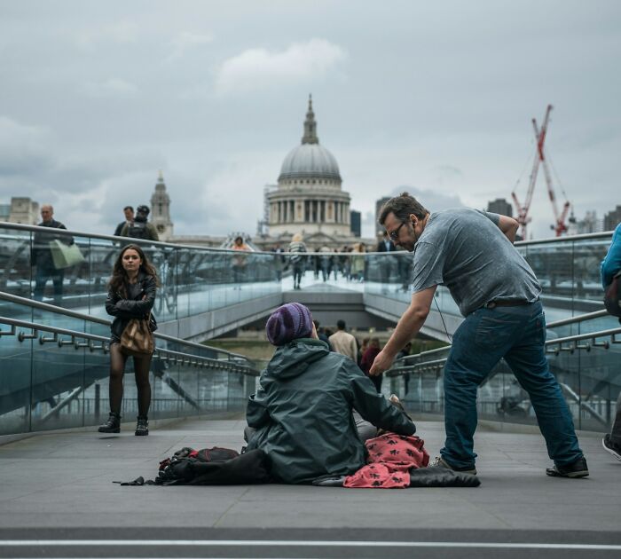 A man assisting someone on a bridge in London, illustrating a real-life human interaction ignored by Hollywood.