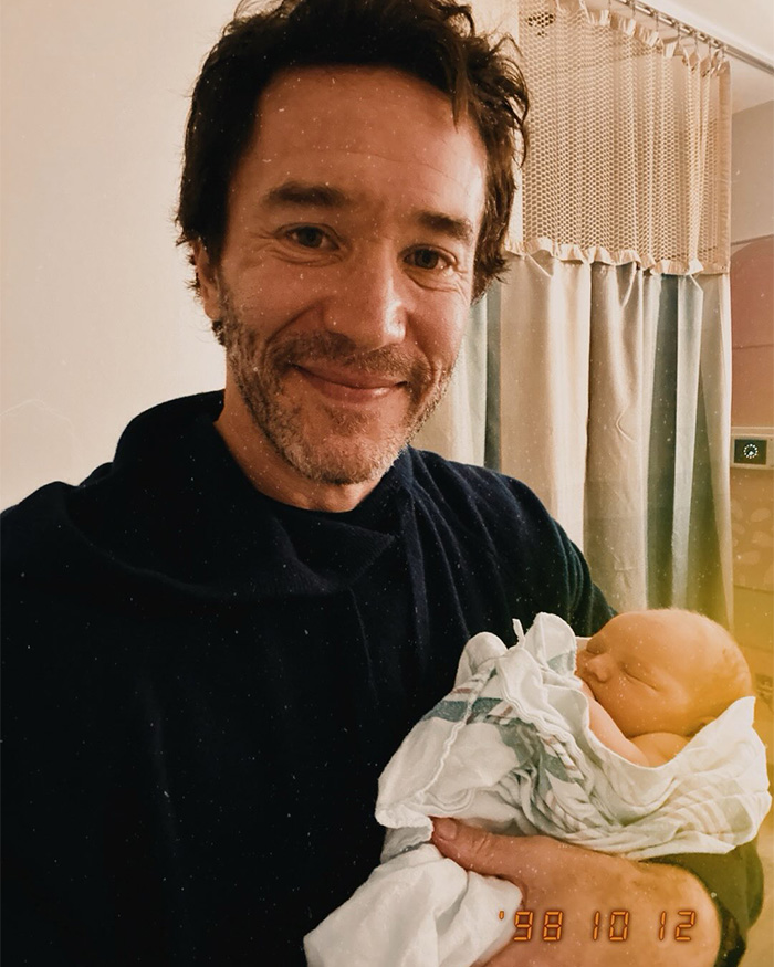 Man smiling while holding newborn baby wrapped in hospital blanket Man smiling while holding newborn baby wrapped in hospital blanket