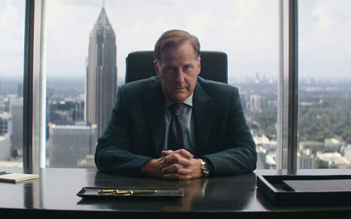 Jeff Daniels seated at a executive desk in a scene from the Netflix miniseries.