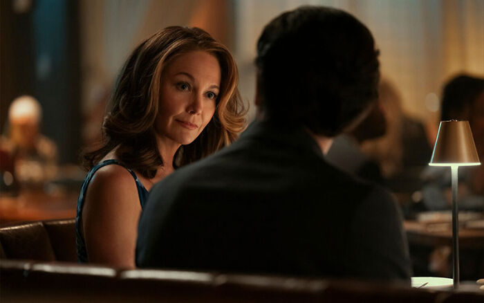 A woman sitting at a dimly lit restaurant table during a conversation in a Netflix miniseries