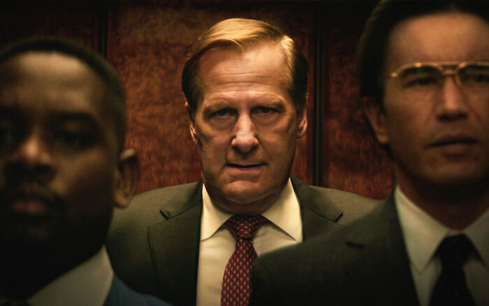Three men in business suits looking forward inside an elevator in a dramatic scene from a Netflix miniseries