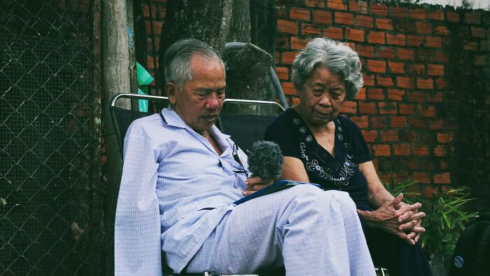 Elderly couple sitting outside with somber expressions