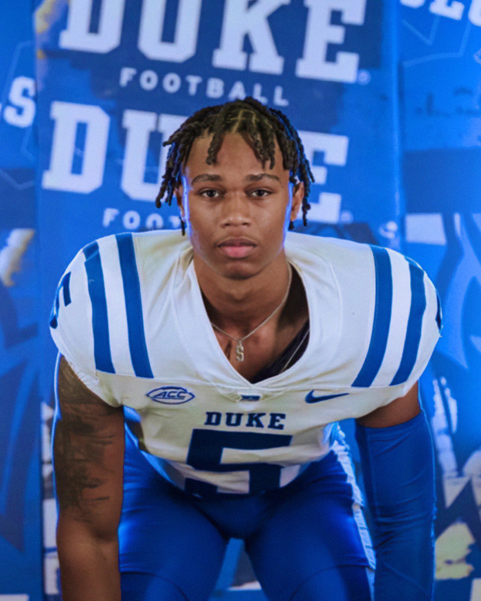 Star football player in Duke uniform posing for portrait in front of Duke football backdrop